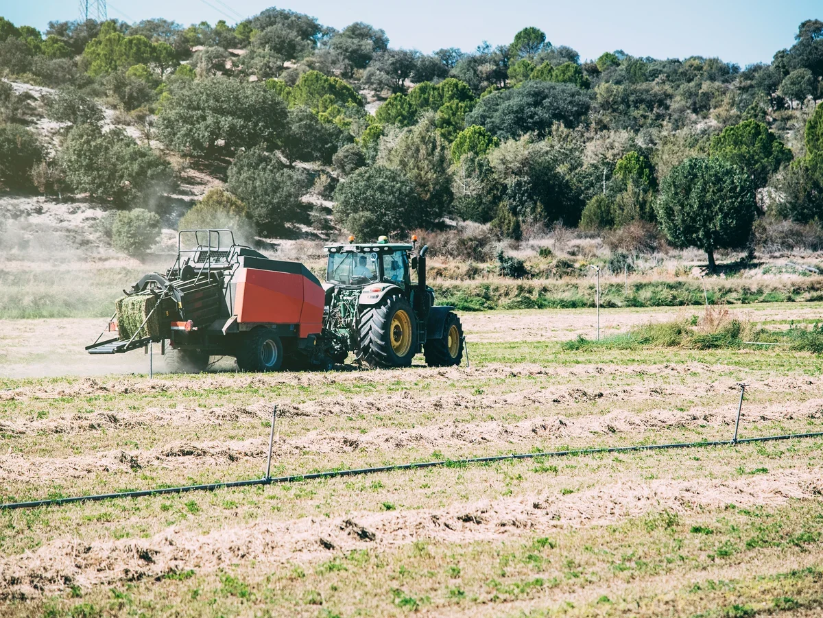 Trabajos agrícolas en el campo Tractor agrícola trabajando en un campo con maquinaria para recoger forraje