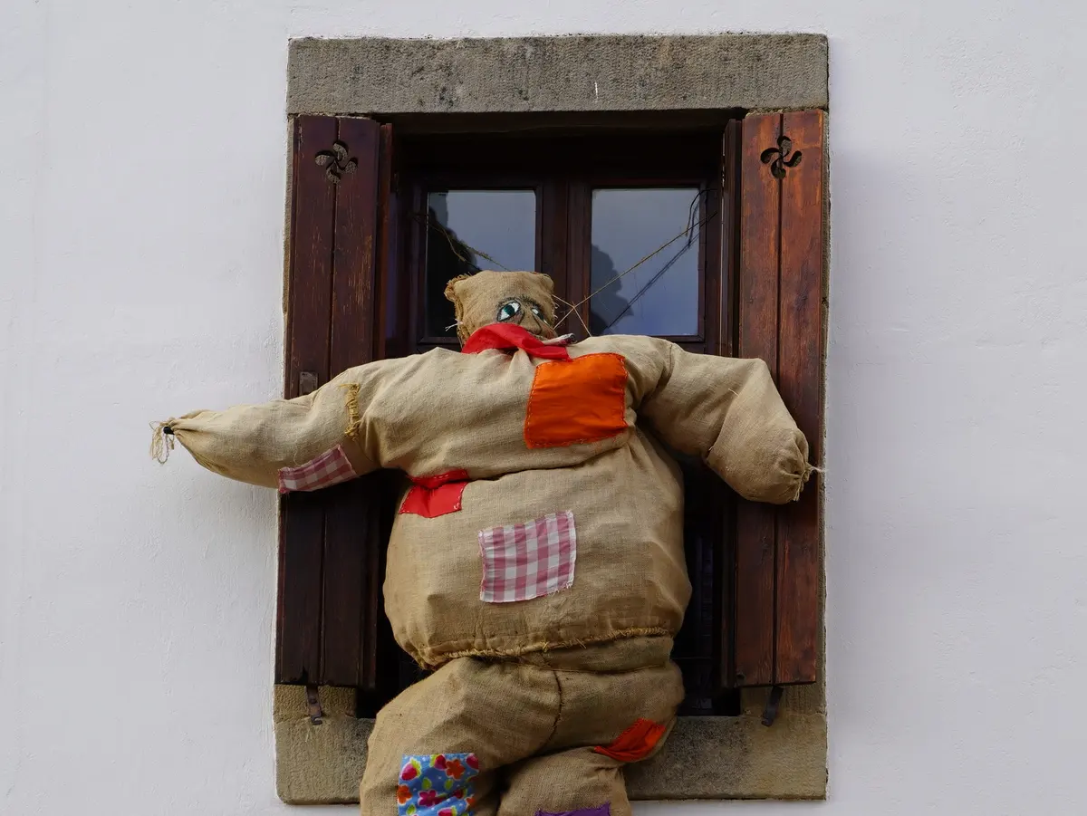 Figura de carnaval en Araia Figura de carnaval confeccionada con tela de saco y parches de colores en una ventana de Araia, Asparrena