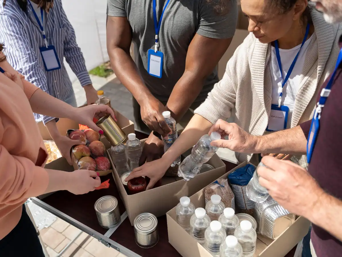 Personas voluntarias organizan alimentos y agua en cajas durante una actividad solidaria