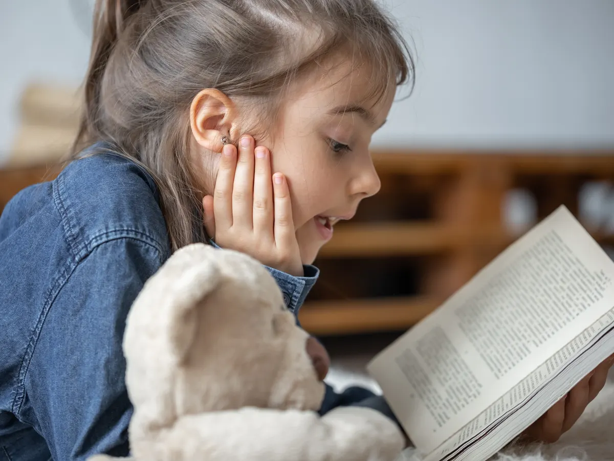 Lectura infantil Niña leyendo un libro junto a un peluche, imagen genérica de promoción lectora