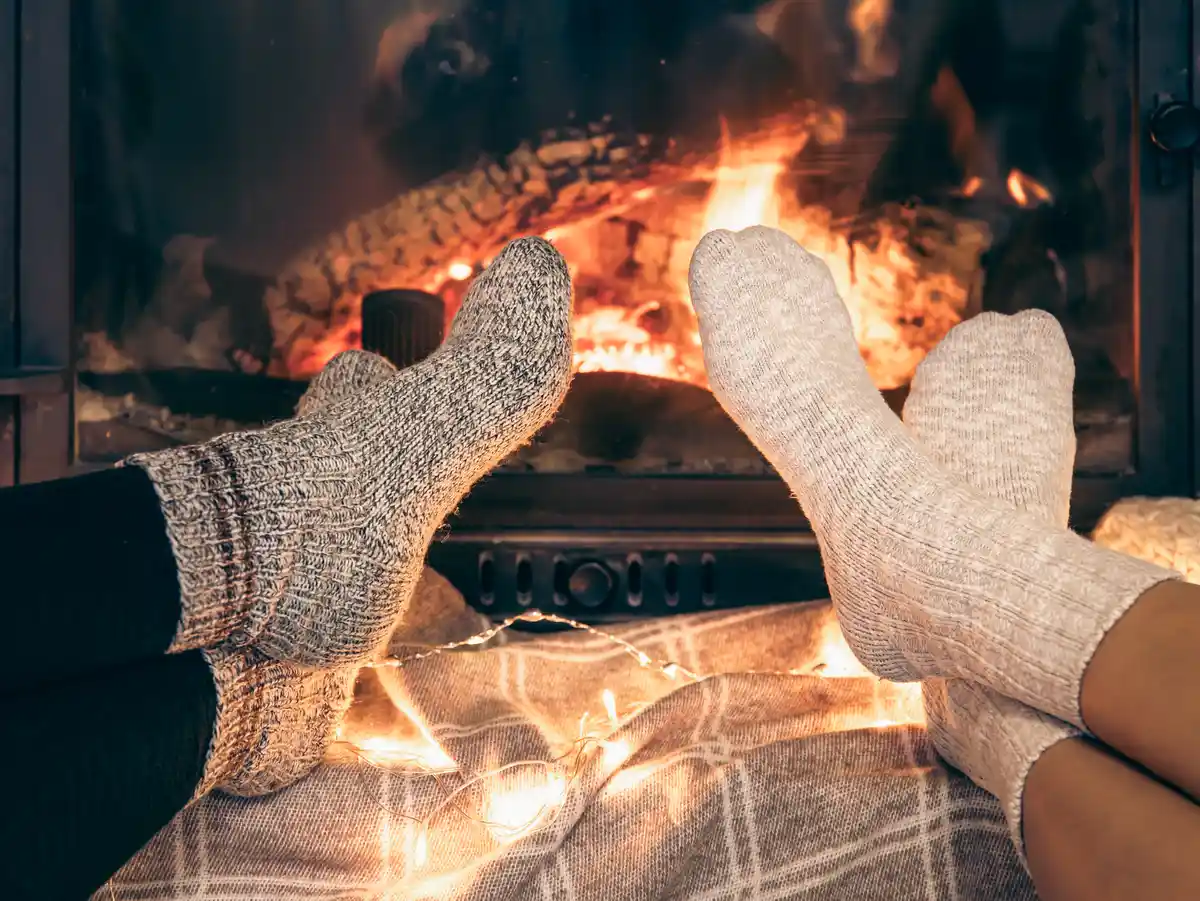 Consejos para revisar y limpiar la chimenea antes del invierno Dos pares de pies con calcetines de lana ante una chimenea encendida